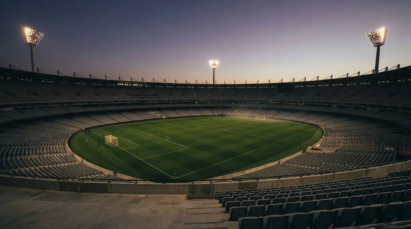 An empty football stadium with floodlight masts at dusk